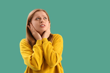 Young woman suffering from loud noise on green background