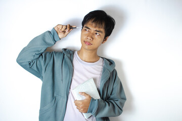 Asian teenager in a white t-shirt and blue hoodie, is in a thinking pose and embracing a book