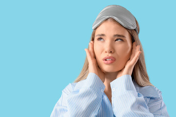 Young woman in pajamas suffering from loud noise on blue background, closeup