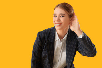 Young businesswoman trying to hear something on yellow background