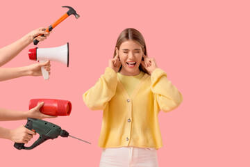 Young woman suffering from loud noise and hands with items on pink background