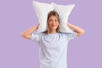 Young woman with pillow suffering from loud noise on lilac background