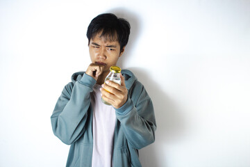 Asian teenager in white t-shirt and blue hoodie, posing focused on observing his glass bottle