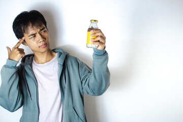 Asian teenager in white t-shirt and blue hoodie, posing in thought with his hand pointing to his head and focusing on his glass