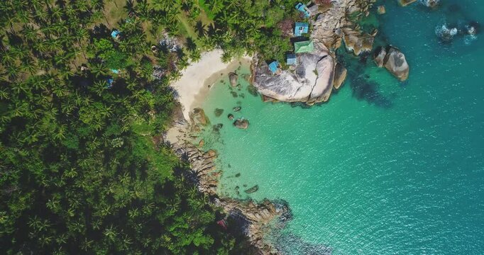 Aerial view of a tropical beach landscape with lush greenery, white sandy shore, turquoise water waves surrounded by rocks. Nature vacation concept. Thailand, Koh Phangan Island, Haad Thong Reng Beach