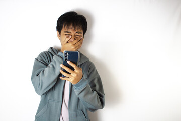 Asian teenager in white t-shirt and blue hoodie, posing sadly looking at the contents of his cellphone