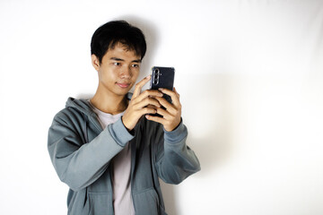 Asian teenager in white t-shirt and blue hoodie, posing taking pictures with his cellphone