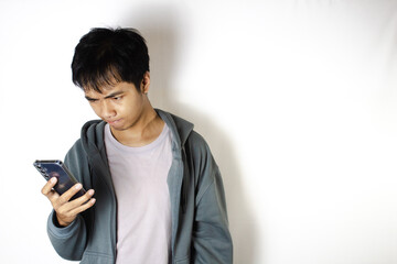 Asian teenager in white t-shirt and blue hoodie, posing focused on looking down at his cellphone