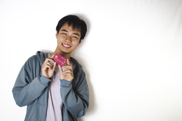 Asian teenager in white t-shirt and blue hoodie, posing holding his credit card