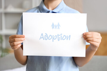 Girl holding paper with word ADOPTION at home, closeup