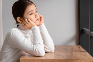 Sad girl at table in room. Adoption concept