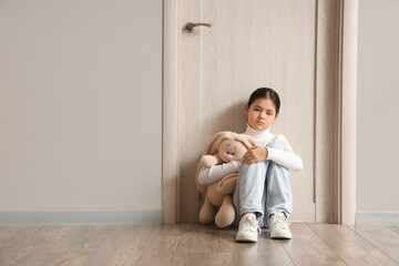 Sad girl with toy bunny sitting near door in hallway. Adoption concept