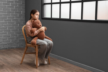Sad girl with toy bear sitting on chair in room. Adoption concept