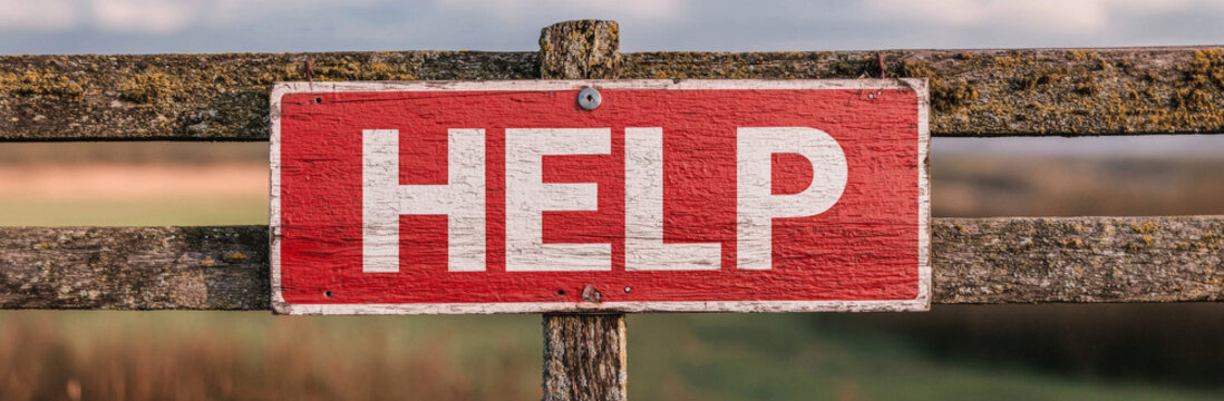 Red help sign on wooden fence in rural area, conveying urgency and need