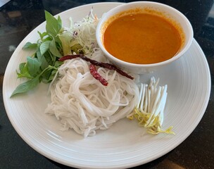 Thai Rice Noodles in spicy Fish curry on black table,  Kanom Cheen Num Ya ,Fresh Thai rice noodle and a fish based sauce, Served with vegetables, dried chillies and basil. Thai food