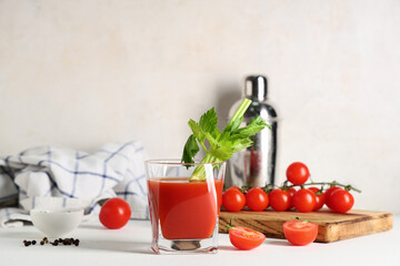 Glass of bloody mary with celery, tomatoes and peppercorns on light background