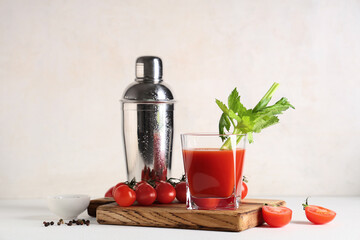 Glass of bloody mary with celery, peppercorns, tomatoes and shaker on light background