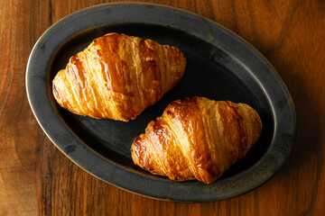 黒い皿に乗せた焼き立てクロワッサン　木製テーブルの背景