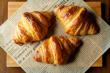 新聞紙風のオーブンペーパーに乗せた焼き立てクロワッサン　木製テーブルの背景