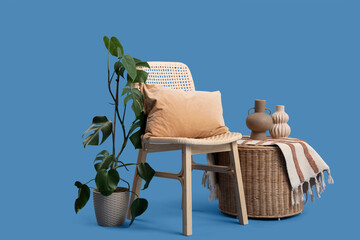 Wooden chair with cushion, houseplant and vases on basket on blue background