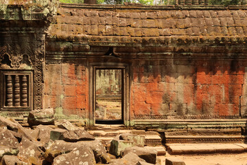 Picturesque view inside the Ta Prohm Temple, a door in a wall covered with red moss, lichens,...