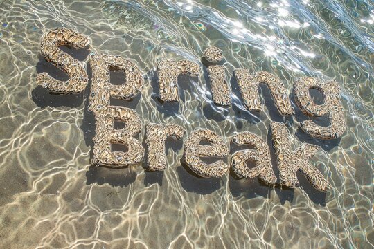 Spring break message formed in sand along the waterline during a sunny beach day