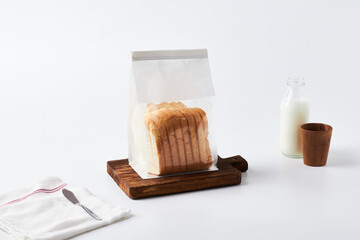 Freshly Packaged Bread and Milk on a Wooden Cutting Board With Utensils in a Bright Kitchen Setting