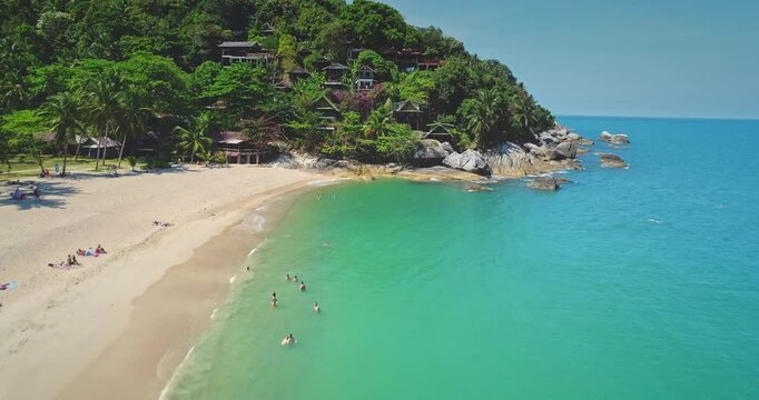 Sandy beach with colorful traditional thai boats, turquoise water, tropical greenery, and relaxing people under a sunny sky, concept of paradise. Thailand, Koh Phangan Island, Haad Thong Reng Beach