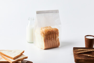 Freshly Packaged Bread With Milk on a Kitchen Table Surrounded by Sliced Bread
