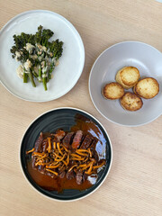 Set of meals of steak, potato, and broccolini.