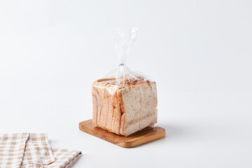 Freshly Packaged Loaf of Bread on a Wooden Cutting Board Against a Light Background