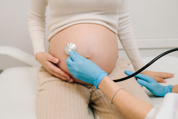 Pregnancy checkup. Gynecologist with stethoscope listening baby's heartbeat in patient's tummy on...