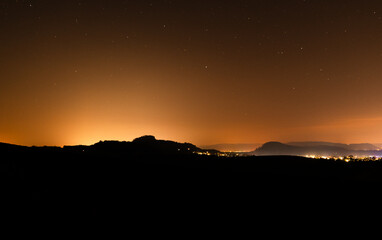 Night view of glowing horizon with distant mountains and city lights illuminating the dark sky