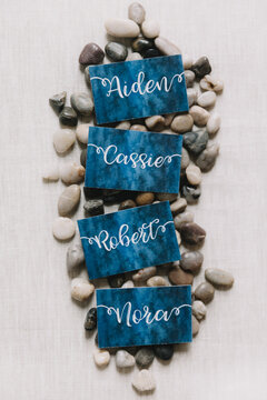 Names written on decorative cards surrounded by smooth pebbles on a light fabric background
