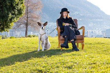 Portrait of a beautiful girl sitting in an armchair in a public park with a very obedient dog next...