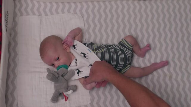 New Born Baby in a Crib While Fathers Hand Calms him Down