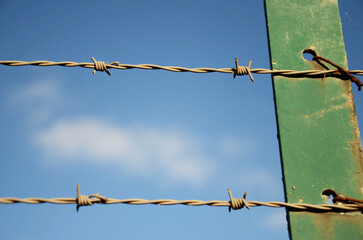 Close-Up of Barbed Wire Fence on a Rusty Metal Post Against a Blue Sky