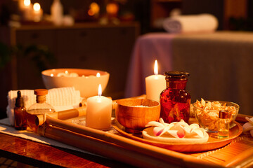 Medium close up of wooden tray with lit soy wax candles and jars with aroma oils on coffee table