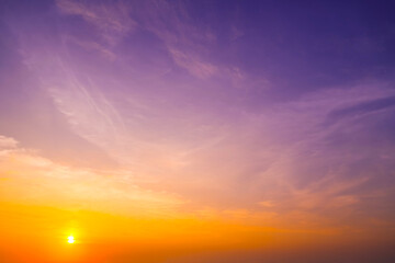Bright orange and purple colors fill the sky as the sun sets beyond the horizon. Soft clouds create a tranquil atmosphere, reflecting the beauty of nature at dusk