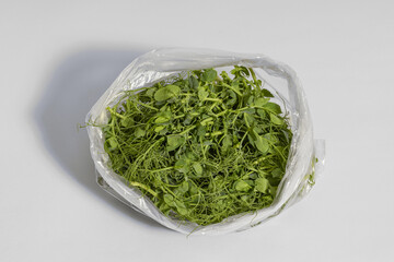 cut pea microgreens weighing 50 grams placed in a plastic bag and prepared for storage on a gray background