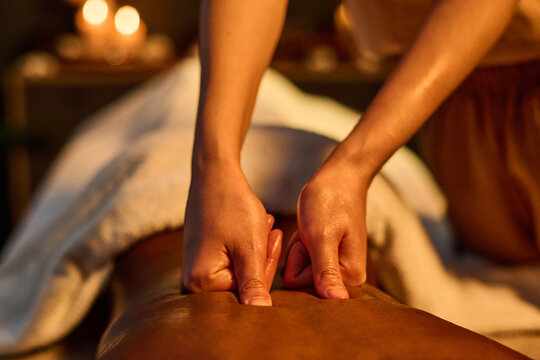 Medium close up of unrecognizable oiled thumbs kneading back muscles to reduce delayed onset muscle soreness