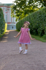 Young caucasian girl in pink dress dancing on pathway in summer garden