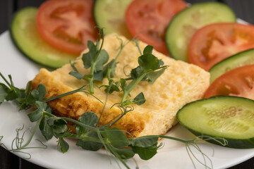 Close-up of a quiche slice with fresh tomato, cucumber, and pea shoots on a white plate