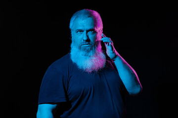 Man with a pink and blue neon-lit beard making a thoughtful gesture, dark background, holding...