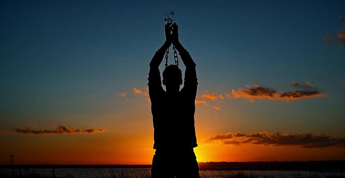Silhouette of a man breaking chains with arms raised against a dramatic cloud sky at sunset, symbolizing freedom and emotional expression