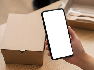 Person Holds Smartphone and Coffee Cup by Laptop in Minimalist Workspace. Hands of an individual holding a smartphone and coffee cup, positioned in front of a minimalist laptop setup with a soft beige