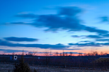 The image shows an evening landscape with buildings, trees, and a sky that transitions from light blue to pinkish-orange. The sun has already set below the horizon, but its reflections are still visib