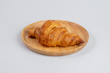 Freshly baked croissant on wooden plate, showcasing its flaky texture and golden color, perfect for breakfast or snack