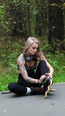 Fototapeta premium Cute blonde puts on roller skates. She feels free and light while roller skating alone in the city park. Stunning Caucasian woman with a beautiful figure uses roller skates for outdoor sports.