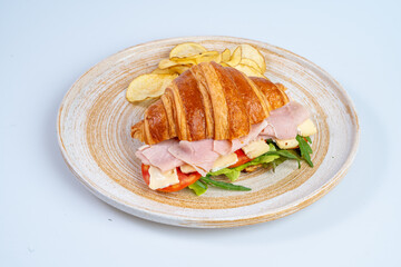 delicious croissant sandwich filled with ham, cheese, and fresh vegetables, served with crispy potato chips on rustic plate